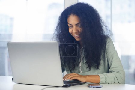 Photo for Happy black woman working on computer. Cheerful African person doing work on laptop at home - Royalty Free Image