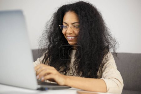 Foto de Mujer feliz escribiendo texto en el teclado de la computadora. Alegre persona femenina que trabaja en el ordenador portátil en casa - Imagen libre de derechos