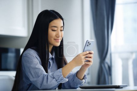 Téléchargez les photos : Heureuse fille asiatique tapant sms message sur l'application de téléphone mobile. Femme vietnamienne joyeuse communiquant en ligne avec smartphone - en image libre de droit