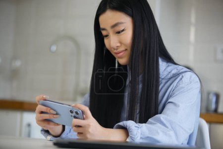 Téléchargez les photos : Asiatique fille jouer à des jeux sur smartphone. Jeune vietnamienne femelle joue jeu vidéo en ligne sur gadget - en image libre de droit