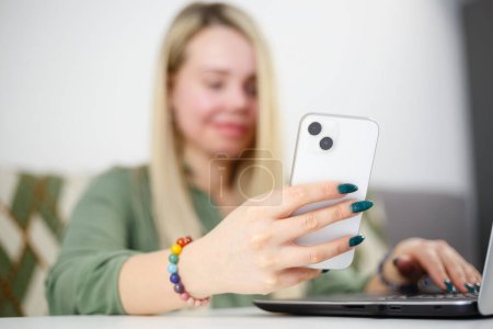 Foto de Mujer joven navegando aplicación móvil en el teléfono inteligente moderno. Rubia persona femenina utilizando el teléfono móvil blanco - Imagen libre de derechos