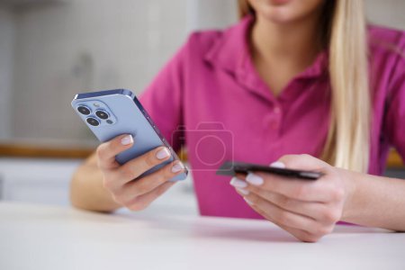 Foto de Mujer pagando en aplicación móvil con tarjeta de crédito. Mujer joven hace tranfser dinero en línea con aplicación de teléfono inteligente y tarjeta bancaria - Imagen libre de derechos