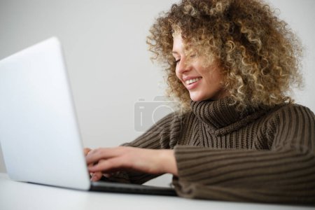 Téléchargez les photos : Heureuse femme blanche tapant du texte sur le clavier de l'ordinateur portable. Femme ukrainienne joyeuse travaillant sur ordinateur portable - en image libre de droit