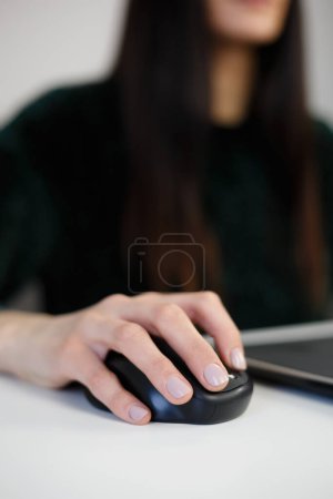 Foto de Mujer haciendo clic con el ratón mientras trabaja en el ordenador portátil. Joven mujer clics con manipulador inalámbrico - Imagen libre de derechos