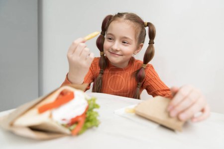 Photo for Cute little girl eats fries and gyros pita sandwich in a Greek restaurant. Adorable white kid eating fast food for lunch in a diner - Royalty Free Image