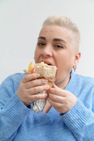 Photo for White woman with short hair enjoying Greek gyro sandwich. Portrait of a hungry female person eating gyros pita snack for lunch - Royalty Free Image