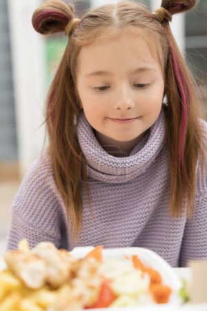 Photo for Hungry little girl looking at food on the table. Portrait of adorable white kid ready to take a bite of fast food for lunch in a cafe - Royalty Free Image