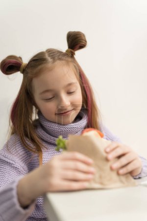 Photo for Cute little girl with ponytails biting a sandwich. Adorable white kid eating lunch meal in a fast food restaurant - Royalty Free Image
