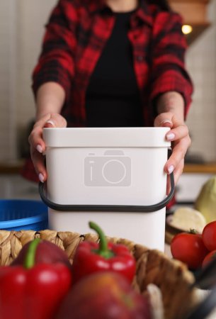 Housewife using compost bin in a domestic kitchen. Female person holds plastic container with bokashi ferment for organic waste. Sustainable lifestyle concept