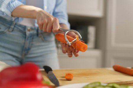Foto de Mujer pelando zanahoria con una herramienta peladora en primer plano. Persona femenina cocinando comida vegetariana saludable con verduras frescas en casa - Imagen libre de derechos