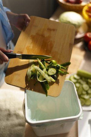 Téléchargez les photos : Cuire en jetant les pelures de concombre dans un bac à compost. Femme cuisinant de la salade verte fraîche à la maison et compostant des déchets organiques dans un récipient bokashi - en image libre de droit