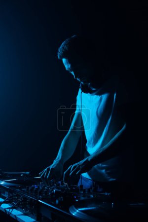 Photo for Silhouette of techno DJ playing music in night club. Cool young white man mixing musical tracks on stage - Royalty Free Image