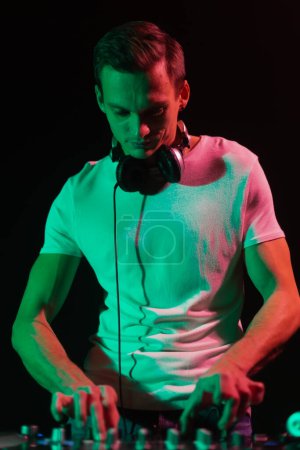Photo for Portrait of young DJ mixing music on party in green light. Cool male person performing on stage as a disc jockey - Royalty Free Image