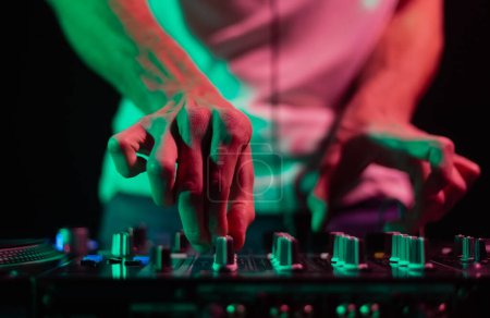Téléchargez les photos : Mains de DJ club mélangeant la musique avec l'appareil de mixage audio en gros plan. Disque jockey professionnel jouant ensemble sur techno partie en boîte de nuit - en image libre de droit