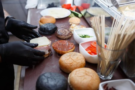 Téléchargez les photos : Cuisinez des hamburgers dans un restaurant de restauration rapide. Travailleur de cuisine portant des gants noirs cuisiner des hamburgers dans un restaurant - en image libre de droit
