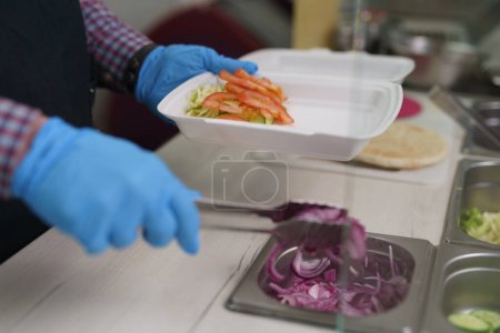 Foto de Cocina preparando comida saludable para llevar en un restaurante griego. Trabajador de cocina preparando plato tradicional kalamaki con verduras frescas - Imagen libre de derechos