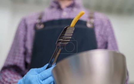 Foto de Cocinar tiene tazón con papas fritas. Trabajador de restaurantes de comida rápida preparando papas fritas para el almuerzo - Imagen libre de derechos