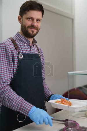 Téléchargez les photos : Portrait d'un homme blanc joyeux cuisinant un plat grec kalamaki dans un restaurant de restauration rapide - en image libre de droit