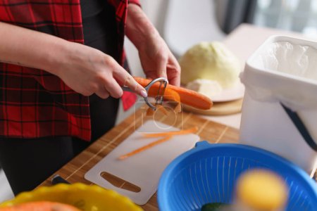 Foto de Cocine pelando la zanahoria con una herramienta peladora. Persona femenina cocinando comida vegetariana saludable en casa - Imagen libre de derechos