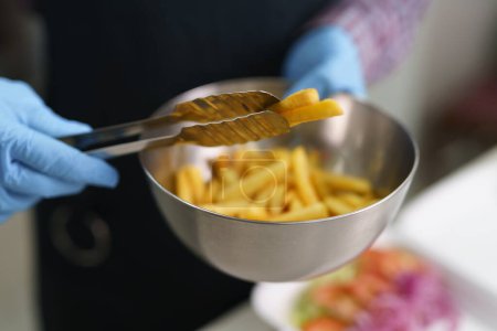 Téléchargez les photos : Le cuisinier servant des frites avec des pinces. Restauration rapide travailleur préparant boîte à lunch pour emporter - en image libre de droit