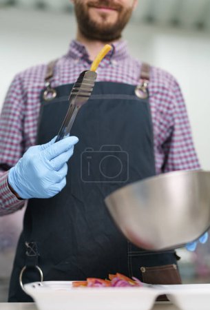 Foto de El cocinero que sirve papas fritas en una lonchera en un restaurante de comida rápida. Hombre alegre trabajando en un restaurante - Imagen libre de derechos