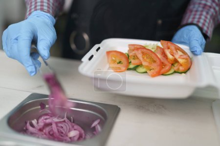Foto de El cocinero toma anillos de cebolla roja española con pinzas de metal. Chef preparando saludable almuerzo vegetariano para llevar - Imagen libre de derechos