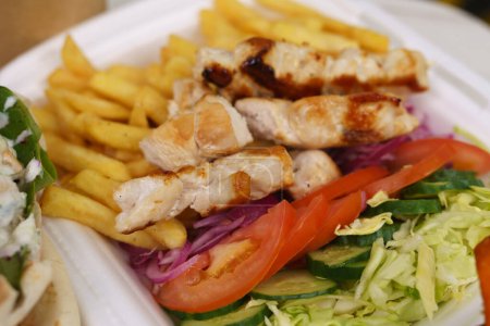 Foto de Almuerzo con carne de cerdo asada, verduras frescas y papas fritas. Comida griega tradicional servida para llevar - Imagen libre de derechos