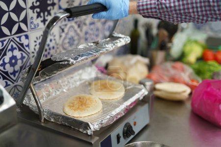 Photo for The cook preparing pita bread on a electric grill in a commercial kitchen. Chef cooking traditional Greek gyros sandwiches for take away in a diner - Royalty Free Image