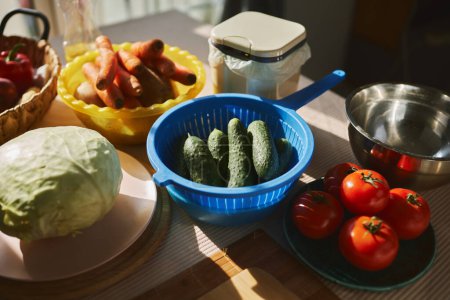 Foto de Verduras frescas preparadas para cocinar. Pepinos, tomates, zanahorias y repollo en la mesa de la cocina - Imagen libre de derechos