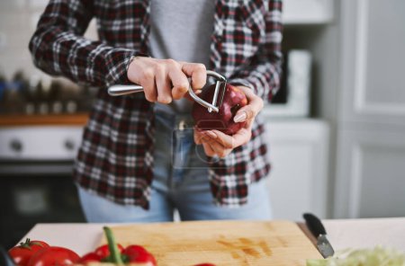 Téléchargez les photos : La cuisinière épluche de près une pomme rouge. Femme utilisant un outil d'épluchage manuel pour préparer des pommes pour manger - en image libre de droit