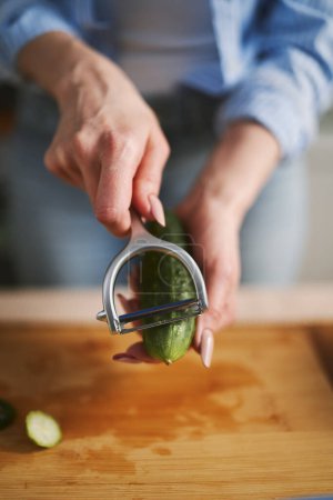 Photo for Woman peeling off a cucumber with a peeler tool in close up. Female person preparing a fresh vegetable salad at home - Royalty Free Image