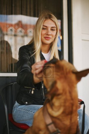Photo for Young blonde woman giving her dog a treat. Cheerful owner feeding th bulldog with snacks. - Royalty Free Image