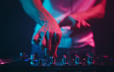 Foto de Manos de un DJ ajustando reguladores de frecuencia de volumen en un mezclador de sonido. disc jockey profesional tocando música en una fiesta en un club nocturno - Imagen libre de derechos