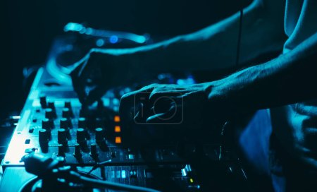 Téléchargez les photos : DJ club jouant de la musique techno sur une fête. Disc jockey mixant des disques vinyles avec un mixeur sur scène - en image libre de droit