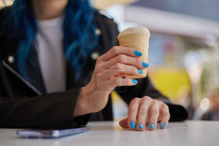 Téléchargez les photos : Une jeune femme dégustant une glace dans un café de rue. Femme méconnaissable tenant un dessert à la main - en image libre de droit