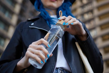 Photo for Young woman drinking water from a glass bottle. Responsible female person using a reusable and ecological bottle to drink liquid - Royalty Free Image