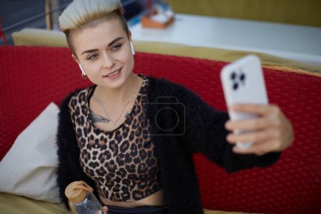 Photo for Beautiful tom boy woman with short hair taking a seflie photo in a restaurant. Cheerful diverse female in leopard clothes posing for a photo in a cafe - Royalty Free Image