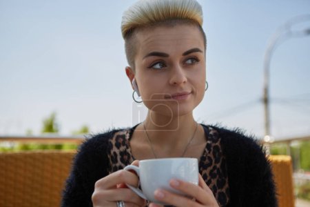 Téléchargez les photos : Portrait d'un beau modèle féminin diversifié avec des cheveux teints courts buvant du thé dans un café extérieur. attrayant tom garçon personne tenant une tasse de café dans les mains - en image libre de droit