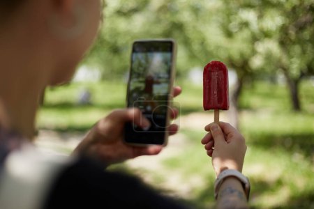 Téléchargez les photos : Jeune fille prenant une photo de crème glacée à la main. Femme méconnaissable prend une photo de dessert avec une caméra de téléphone intelligent - en image libre de droit