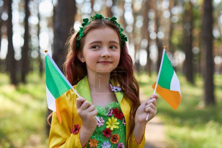 Photo for Pretty little girl celebrating St Patricks Day and waving with flags of Ireland dressed as a fairy - Royalty Free Image