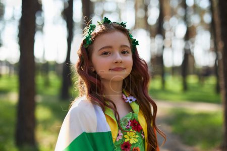 Photo for Saint Patrick's Day images. Portrait of a beautiful little girl with red hair dressed in a green fairy costume and covered with flag of Ireland - Royalty Free Image