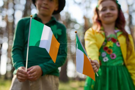 Photo for Kids celebrating St Patricks Day on the 17th of March. Children dressed as leprechauns waving with national Irish flags - Royalty Free Image