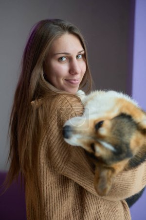 Téléchargez les photos : Belle jeune femme tenant un chien corgi dans les mains. Aimer propriétaire d'animal posant avec un chiot - en image libre de droit