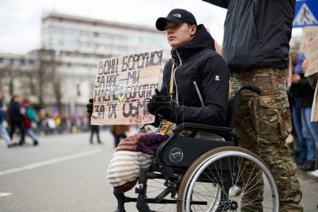 Foto de Soldado ucraniano herido en una silla de ruedas sostiene una pancarta "Ellos lucharon por nosotros. Tenemos que luchar por su liberación "en una manifestación. Kiev - 3 de marzo de 2024 - Imagen libre de derechos