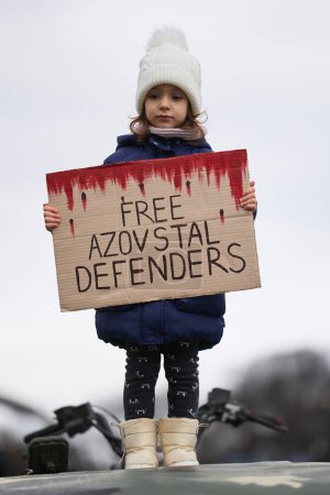 Foto de Niña ucraniana sostiene una pancarta "Free Azovstal Defenders" en la parte superior de un camión militar en una manifestación pacífica en el centro de Kiev - 18 de febrero de 2024 - Imagen libre de derechos