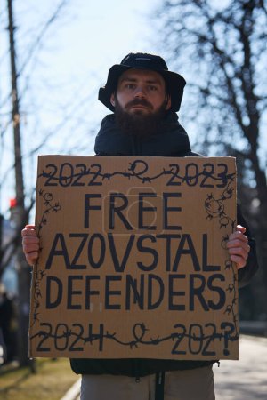 Photo for Young Ukrainian man holds a banner "Free Azovstal Defenders" on a peaceful demonstration dedicated to garrison of Mariupol who remains in russian captivity since 2022. Kyiv - 10 March,2024 - Royalty Free Image