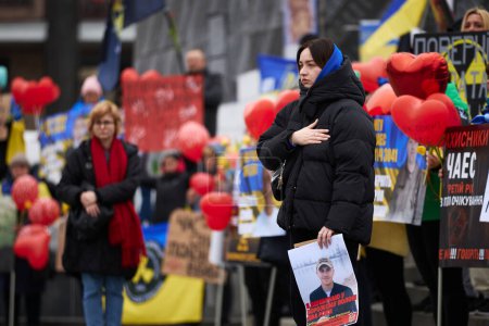 Foto de Mujer ucraniana patriótica con un retrato de su esposo capturado cantando el himno nacional de Ucrania en la manifestación pública. Kiev - 16 de marzo de 2024 - Imagen libre de derechos