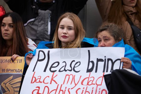 Foto de Mujeres ucranianas posando con una pancarta "Por favor, traigan de vuelta a mi padre" en un mitin por la liberación de soldados capturados de las Fuerzas Armadas de Ucrania de las prisiones rusas. Kiev - 16 de marzo de 2024 - Imagen libre de derechos