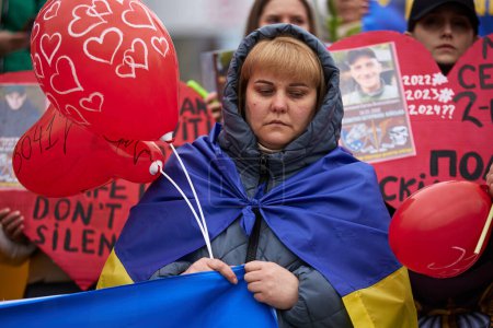 Foto de Triste mujer con bandera nacional ucraniana en hombros en la manifestación pública en la Plaza de la Independencia (Maidan Nezalezhnosti) en Kiev - 16 de marzo de 2024 - Imagen libre de derechos