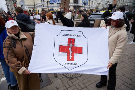 Foto de Trabajadores médicos ucranianos posando con una bandera de Médicos Militares de Ucrania en una reunión pública para la liberación de los militares capturados. Kiev - 17 de marzo de 2024 - Imagen libre de derechos